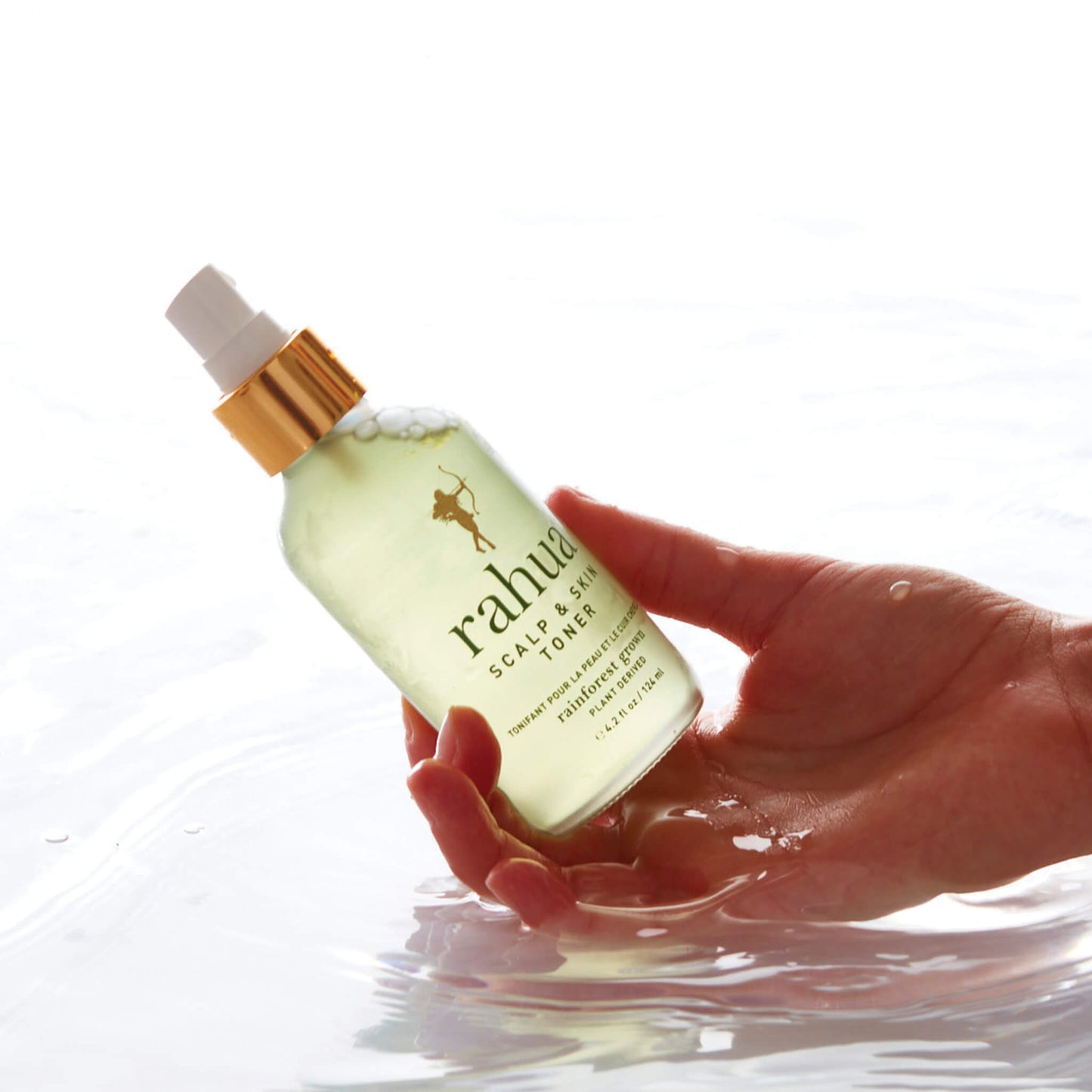 woman holds Rahua Scalp and Skin Toner on right hand on top of water