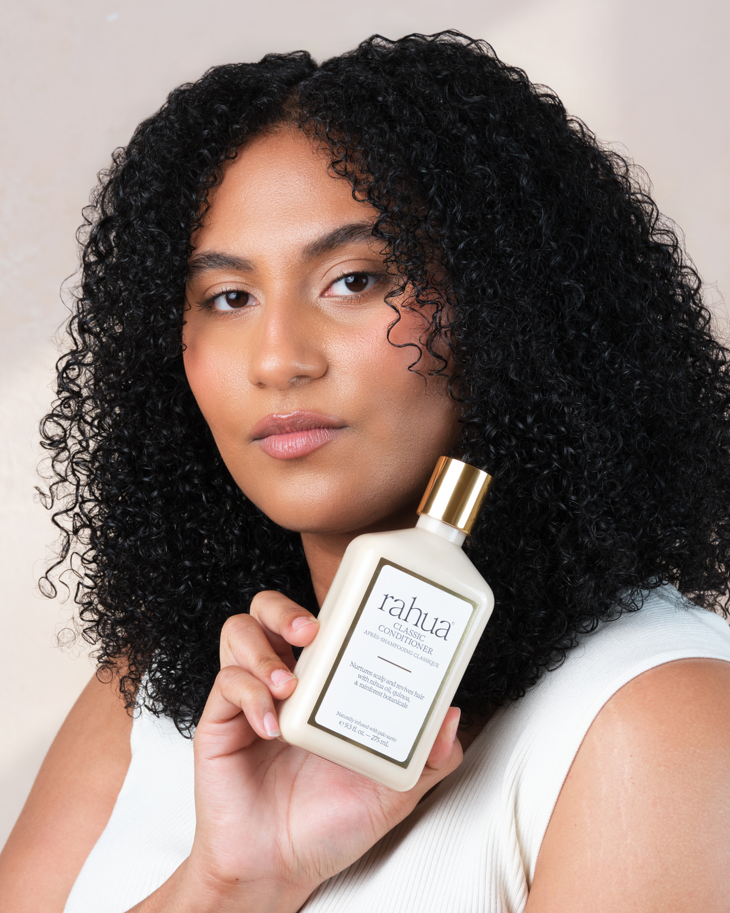 Woman holding a bottle of Rahua hair product against a neutral background|variant:93-oz,18-oz