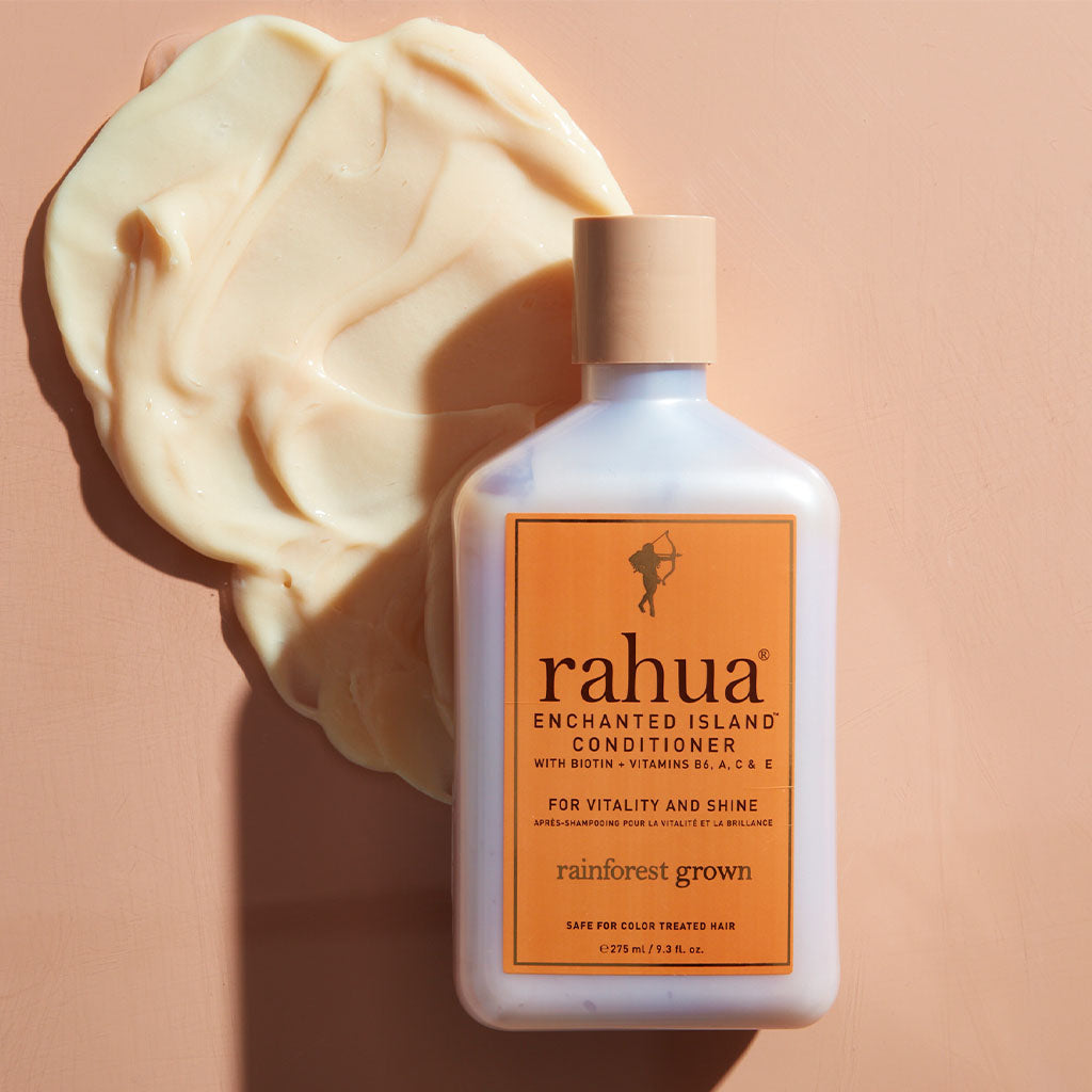 bottle of rahua enchanted island conditioner on a beige orange background with a spread of conditioner under the bottle to show product texture|variant:93-oz