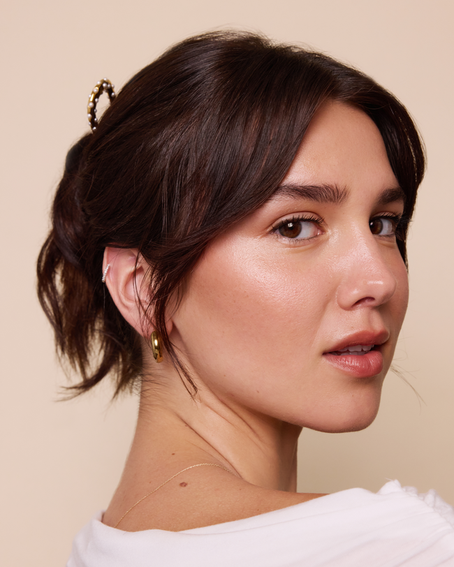 Woman with styled hair and gold earrings against a beige background